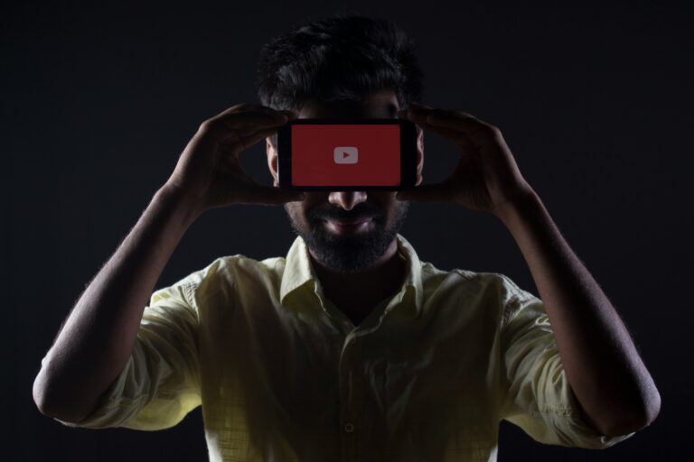 A man is holding a phone in his hand and placing it in front of his eyes; the phone screen displays YouTube.