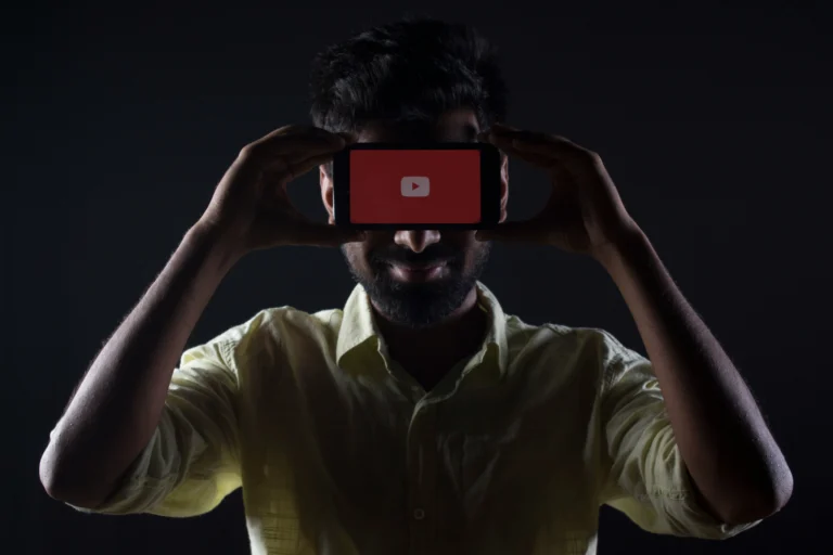 A man is holding a phone in his hand and placing it in front of his eyes; the phone screen displays YouTube.